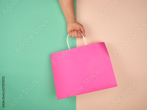 female hand holding a pink paper shopping bag on green beige background