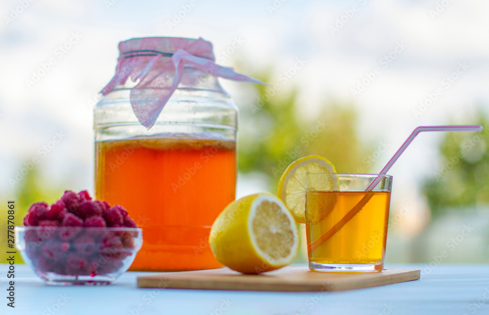 Kombucha in a jar on a light wooden table against the sky, a glass filled with Kombucha with raspberries. Kombucha in a jar on a light wooden table against the sky, a glass filled with Kombucha with raspberries.