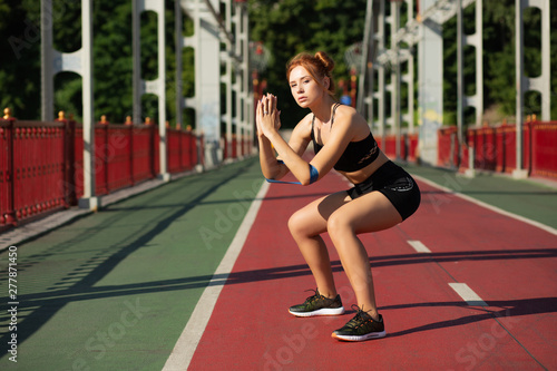 Athletic red haired girl squatting doing sit-ups with elastic resistance band. Empty space