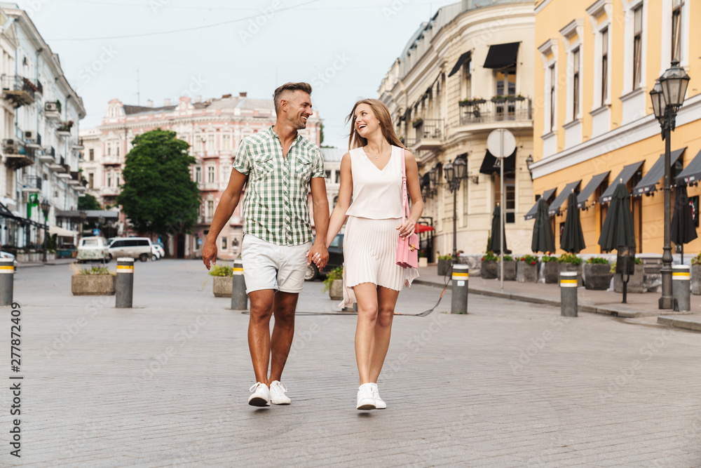 Image of caucasian happy couple smiling and holding hands together while walking through city street Image of caucasian happy couple smiling and holding hands together while walking through city street