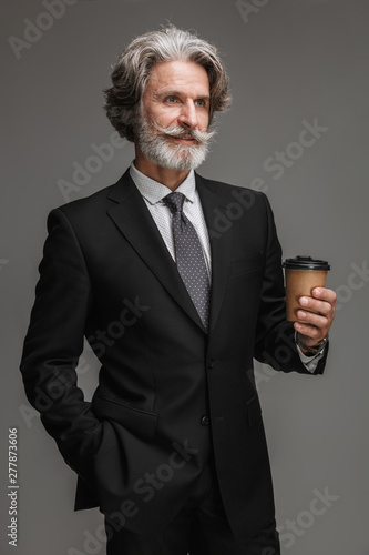 Image of caucasian adult businessman wearing formal black suit smiling and holding paper cup