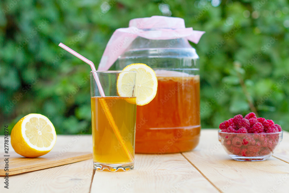 Fototapeta premium Glass jar with Kombucha, poured glass with Kombucha and raspberries in the summer garden.