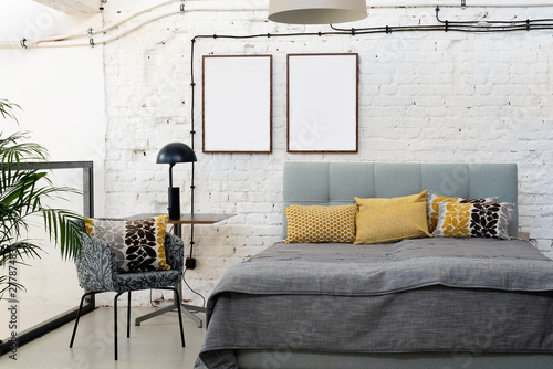 Industrial interior of bedroom in scandinavian style with grey bed, pillows and white bricky wall with blank frames with mock up.