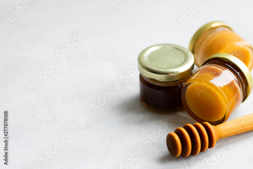 Three small glass jar close up of yellow and brown honey with metal caps and special wooden spoon isolate on grey cement background, copy space. Healthy product natural, Horizontal Selective focus