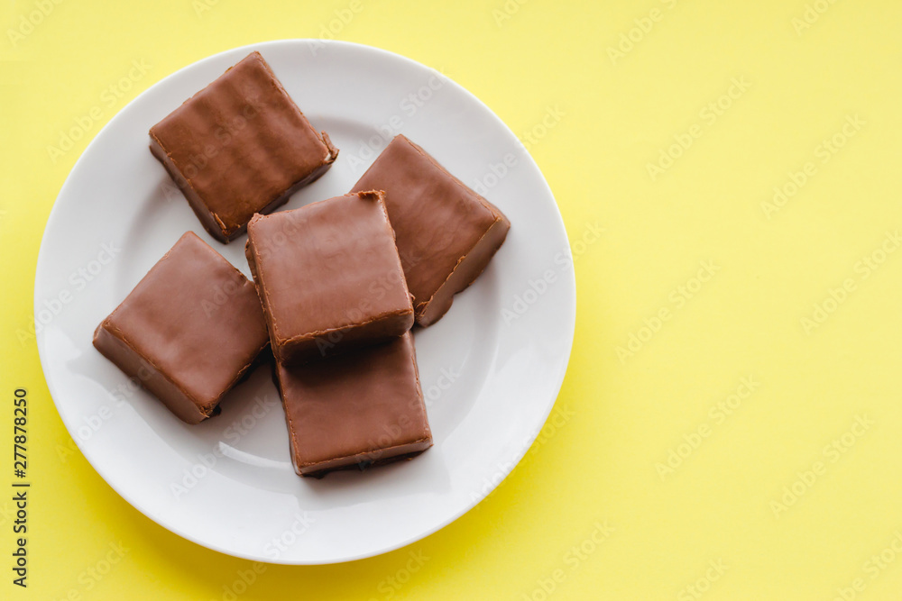Fototapeta premium Chocolate sweets on a plate on a yellow background.