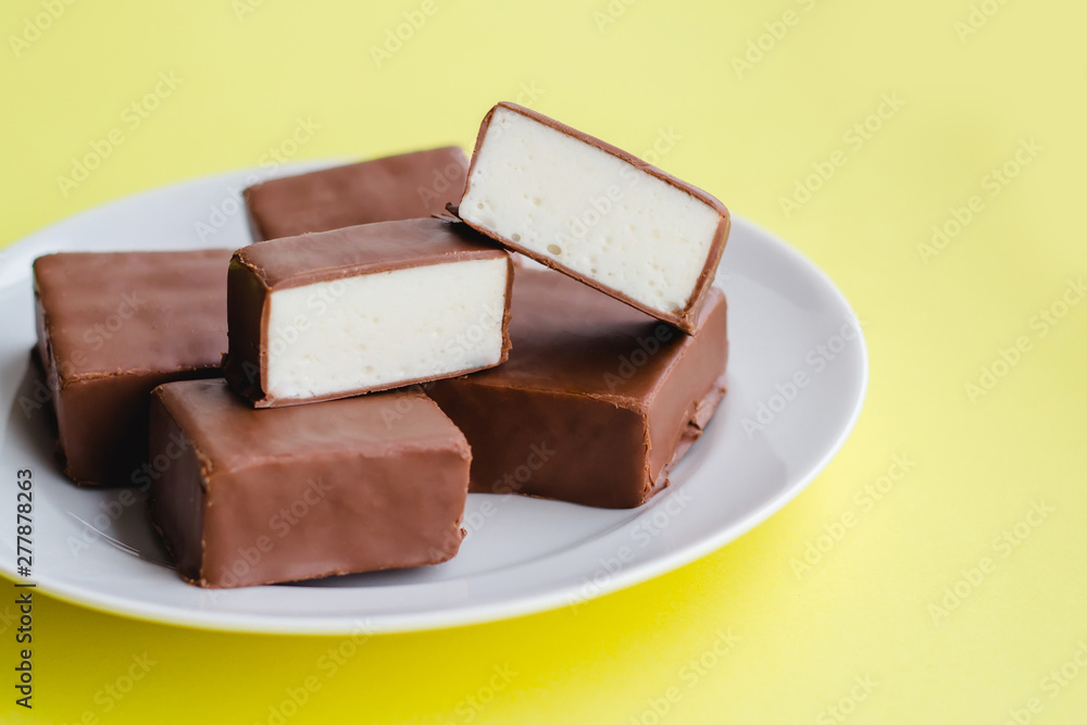 Chocolate sweets with white souffle on a plate on a yellow background. Chocolate sweets with white souffle on a plate on a yellow background.