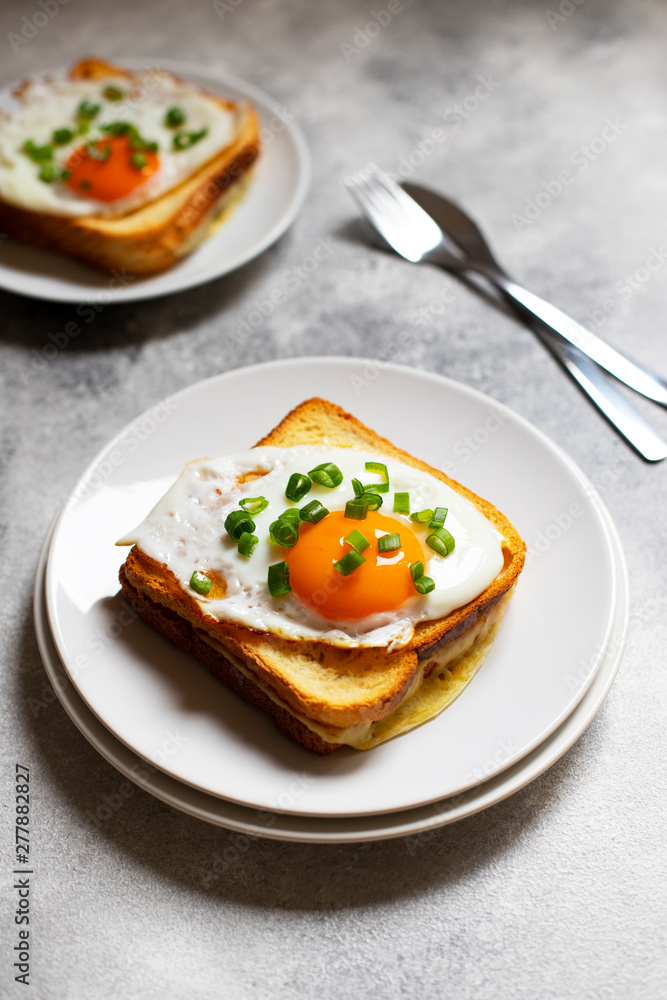 Sandwich with ham, cheese and egg. A traditional French croque-madame sandwich served on a white plate. Popular French cafe meal. Gray background. Close-up. Space for text