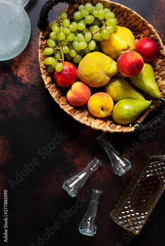 Rakia or Rakija the traditional balkan fruit brandy. The fruits of which produce Rakia. Fruits in a basket, bottles and glasses for alcohol. Top view. Dark vintage background. Space for text photo