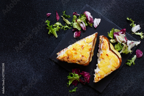 Sandwich with ham, cheese and bechamel sauce. A traditional french croque-monsieur sandwich served with lettuce leaves on a black plate. Black background. Top view. Space for text photo