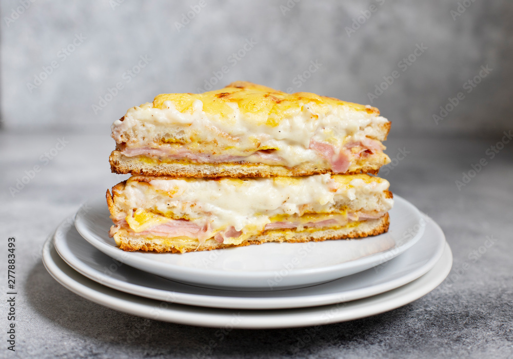 Sandwich with ham, cheese and bechamel sauce. A traditional french croque-monsieur sandwich served on a white plate. Gray background. Close-up. Front view. Space for text Sandwich with ham, cheese and bechamel sauce. A traditional french croque-monsieur sandwich served on a white plate. Gray background. Close-up. Front view. Space for text