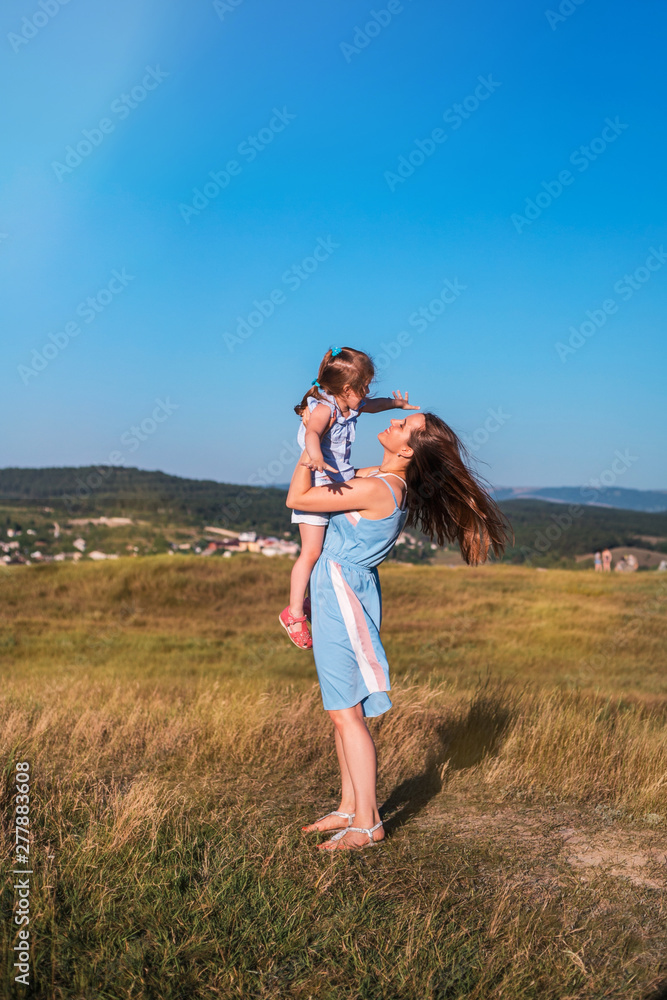 Young mother and daughter have fun and playing in a golden field of sunshine.