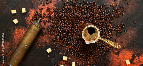 Turkish coffee concept. Copper coffee pot (Cezve), vintage coffee grinder, coffee beans and sugar on a dark vintage background. Banner format. Top view