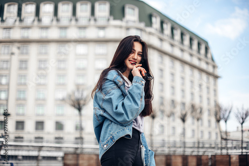 Close up fashion street stile portrait of pretty girl in fall casual outfit walking in city. Beautiful brunette or student enjoying weekends.