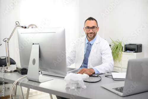 Slika na platnu portrait of a handsome man male doctor in medical practice office working on com