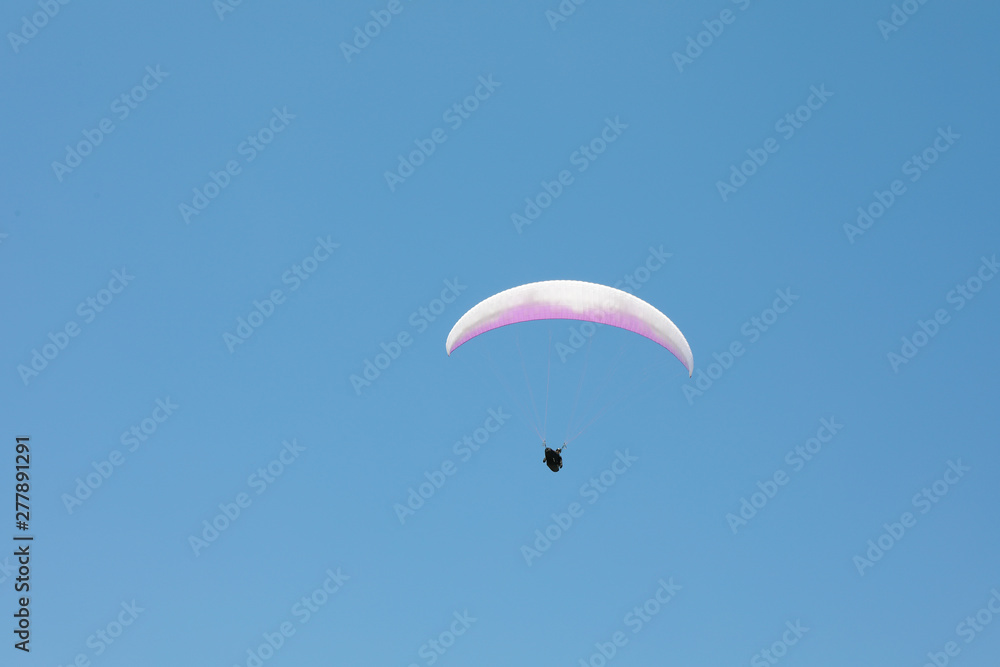 Skydiver with a white-pink parachute flies across the blue sky Skydiver with a white-pink parachute flies across the blue sky