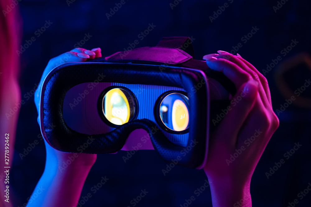 Female hands hold 3d 360 vr headset glasses goggles in futuristic purple neon light, girl gamer virtual augmented ar reality innovative party experience technology background concept, close up view