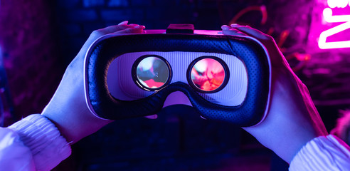 Female hands hold 3d 360 vr headset wear ar innovative glasses goggles on camera in futuristic purple neon light, girl gamer virtual augmented reality technology background concept, close up view