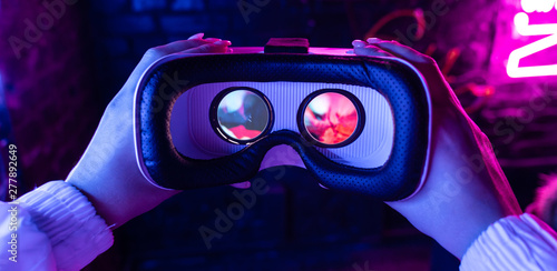 Female hands hold 3d 360 vr headset wear ar innovative glasses goggles on camera in futuristic purple neon light, girl gamer virtual augmented reality technology background concept, close up view