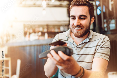 Smiling man making a wireless payment, customer using mobile phone, device with nfc technology for paying the bill photo