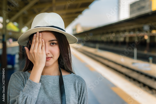 happy young woman closes one eye with his hand, hipster background on train station,summer travel and vacation concept.