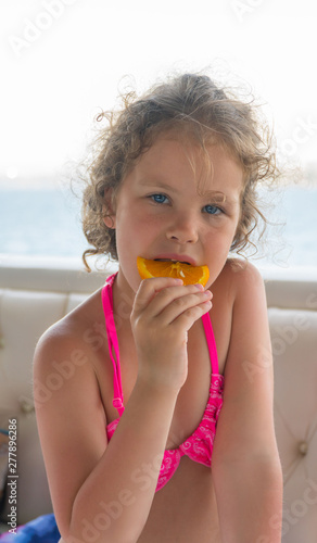 Baby with orange. Happy little girl eating orange near the sea.