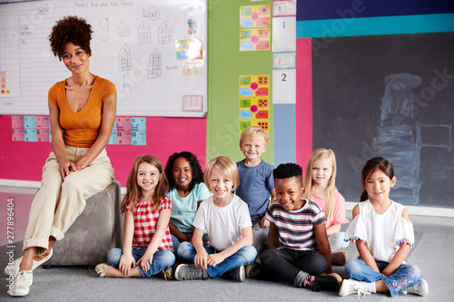 Portrait Of Elementary School Pupils Sitting On Floor In Classroom With Female Teacher