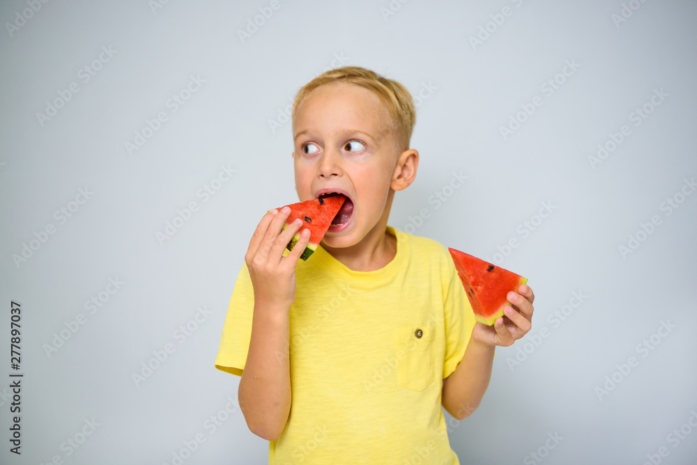 Cheerful caucasian 5 year old boy in yellow t-shirt capering and eating a piece of red watermelon, summer concept. Cheerful caucasian 5 year old boy in yellow t-shirt capering and eating a piece of red watermelon, summer concept.