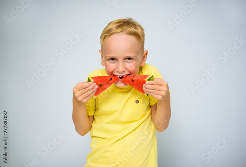 Photography Frolicsome caucasian 5 year old boy without incisor capering and eating pieces of red watermelon, dentist concept