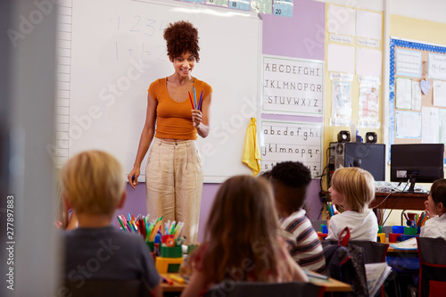 Female Teacher Standing At Whiteboard Teaching Maths Lesson To Elementary Pupils In School Classroom photo