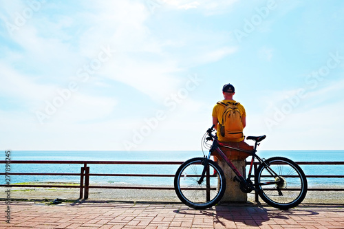 Young man with fit body riding the mtb mountain bike on sandy beach with beautiful azure water sea view. Muscle male wearing bright yellow t-shirt cycling on ocean shore. Close up, copy space.