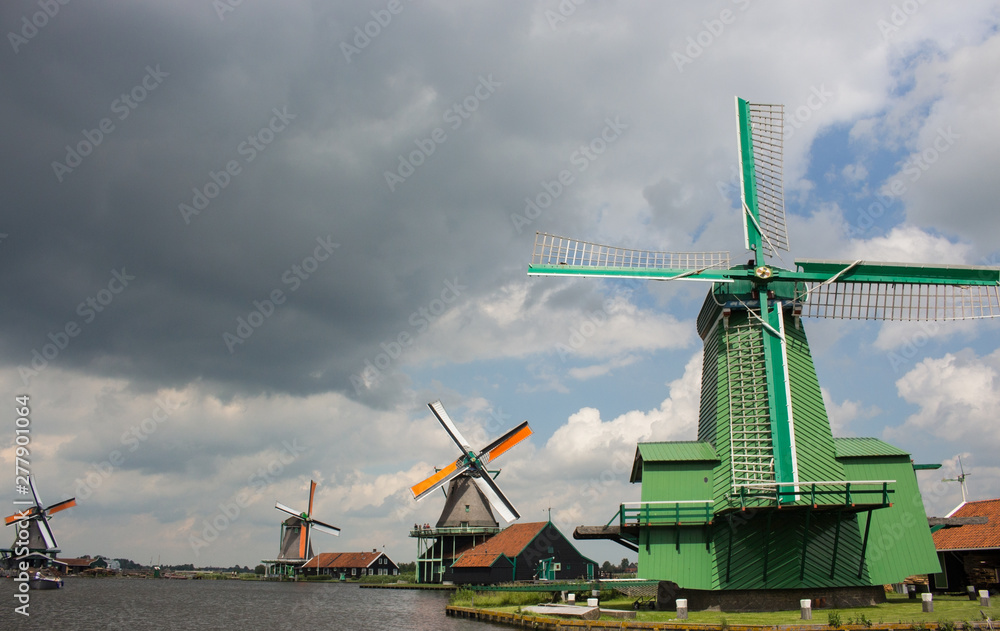 Zaanse Schans, Netherlands - 06/14/2019: Old dutch windmills in historical village. Wooden mills in field with river. Historic architecture in Europe. Rural holland landmark. Wind energy concept. 