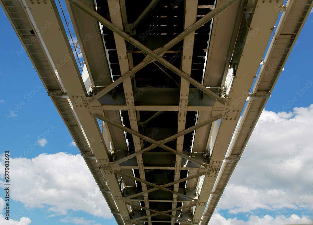 Bottom view of the railway bridge. Metal constructions of the railway bridge, the bottom view. Blue sky and white clouds
