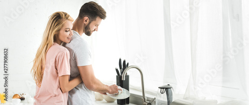 panoramic shot of woman hugging man washing dishes at kitchen