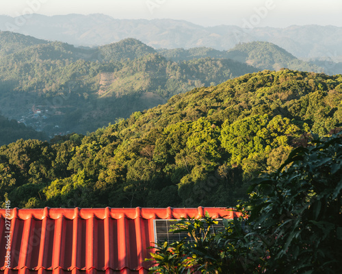 Tree branches on red house roof with solar cell panels and mountain with sunlight and fog in the evening in the Akha village of Maejantai on the hill in Chiang Mai, Thailand. photo