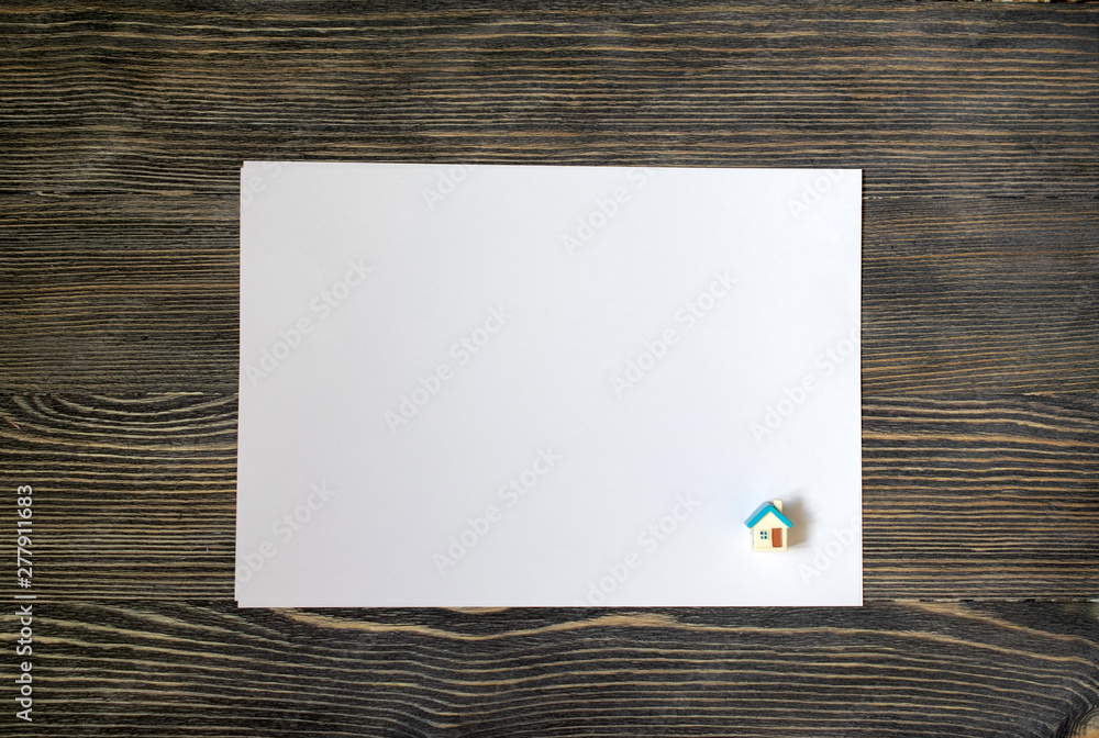 one white sheet of paper and a small house on a wooden background one white sheet of paper and a small house on a wooden background