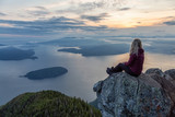 Adventurous Female Hiker on top of a mountain covered in clouds during a vibrant summer sunset. Taken on top of St Mark's Summit, West Vancouver, British Columbia, Canada.