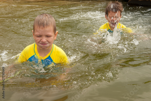 Funny children in swimsuits accelerate on wooden bridge near river and jump into water. boys are happy on holiday in village together. Summer day, river, swimming in water