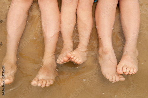 Funny kids in bathing suits sit together on sand with their legs in water. boys are happy on holiday in village together. Summer day, river, swimming in the water. Close-up legs and feet © galitsin