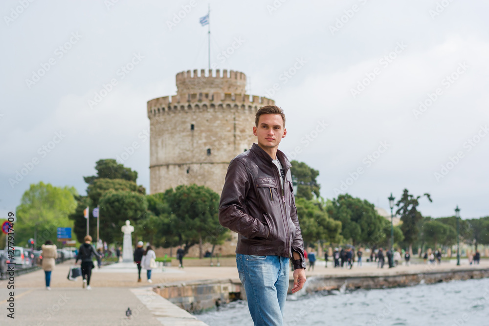 Young handsome man, tourist, stands near a White Tower in the center Thessaloniki, Greece near a sea