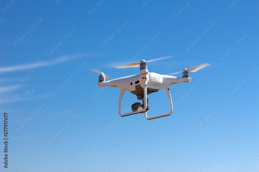 White quadcopter, drone hovering in the sky, bottom view