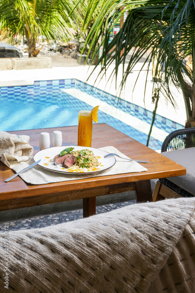 Lamb tenderloin served with a glass of freshly squeezed orange juice, a meal on the table next to the swimming pool