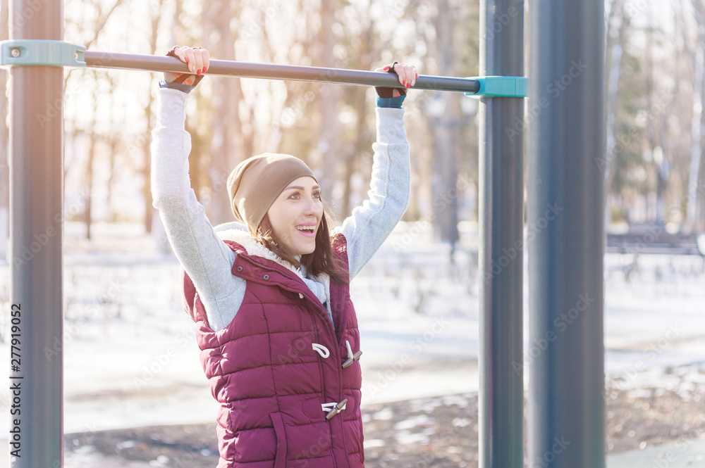 Attractive girl involved in sports workout on a horizontal bar on a sunny winter day. The concept of sports activities all year round Attractive girl involved in sports workout on a horizontal bar on a sunny winter day. The concept of sports activities all year round