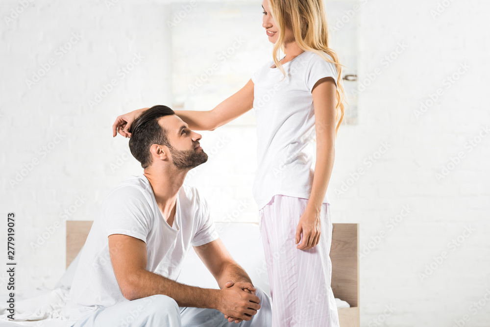 Fototapeta premium beautiful woman in pajamas stroking man in bedroom with sunlight