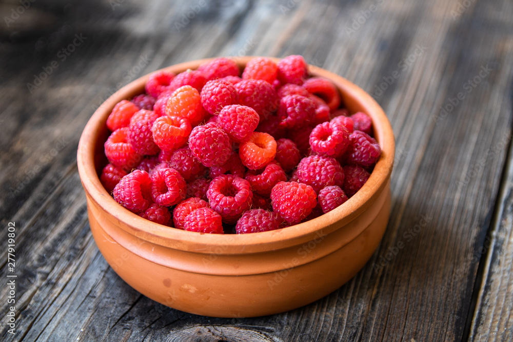 Fresh organic raspberries in a clay bowl on old wooden table Fresh organic raspberries in a clay bowl on old wooden table