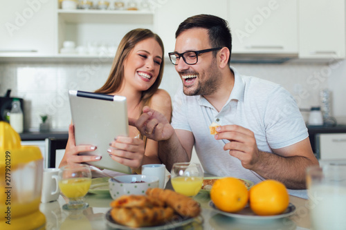Happy couple enjoying breakfast time together at home and using digital tablet.