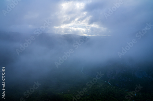 Montenegro, Dark rain clouds and fog hiding beautiful endless green nature landscape of tara river canyon from above a mountain top in the evening