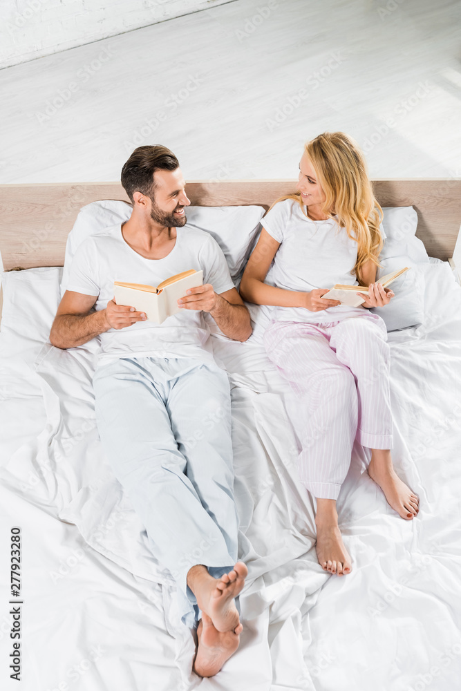 Fototapeta premium beautiful smiling couple lying in bed with books at home