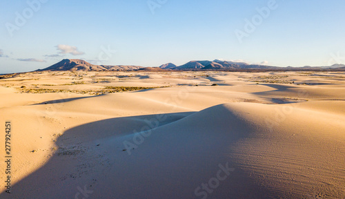 Above view of desert dunes - concept of wild adventure travel destination and beauty of the planet in untouched nature and outdoors - mountains in background and shadows on the sand