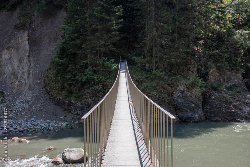 Fototapeta premium View of a wild river in a gorge with a modern hanging bridge in the Swiss Alps