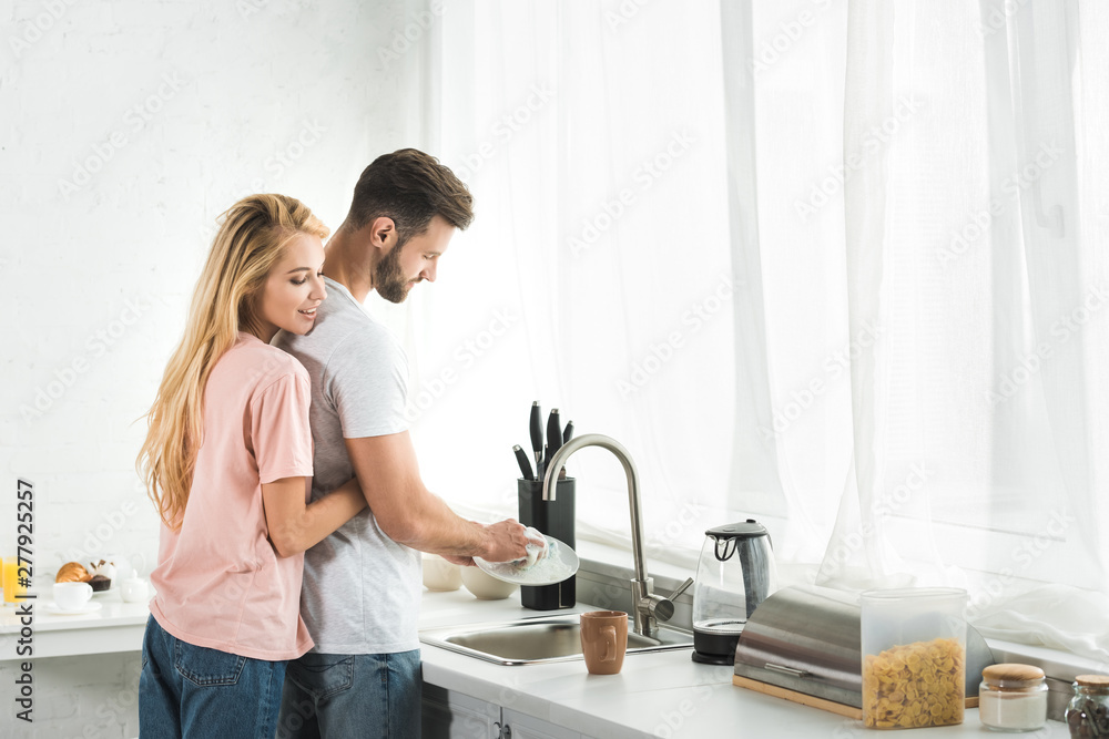 beautiful woman hugging man washing dishes at kitchen beautiful woman hugging man washing dishes at kitchen